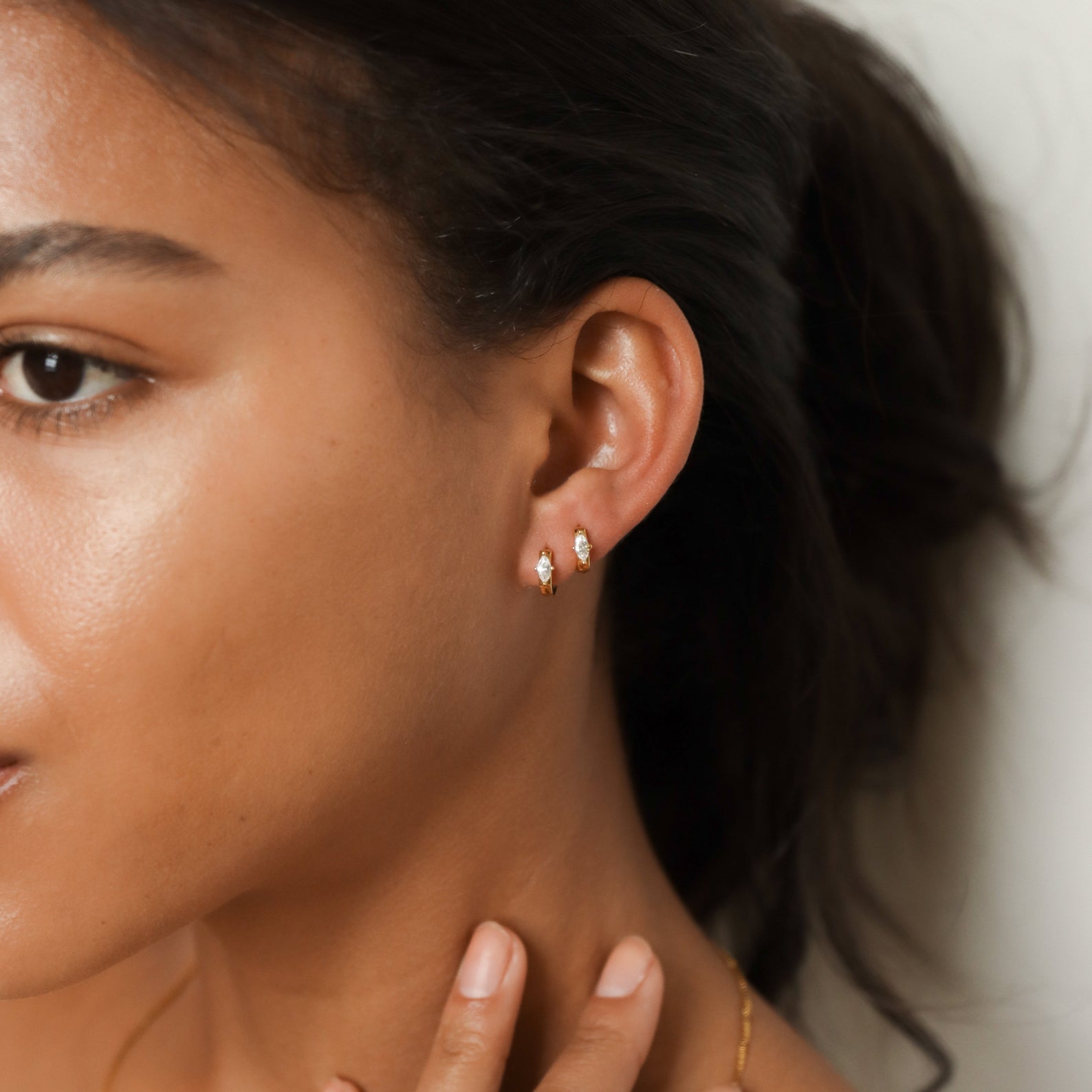 Close-up of a woman wearing gold marquise diamond hoop earrings with a neutral background