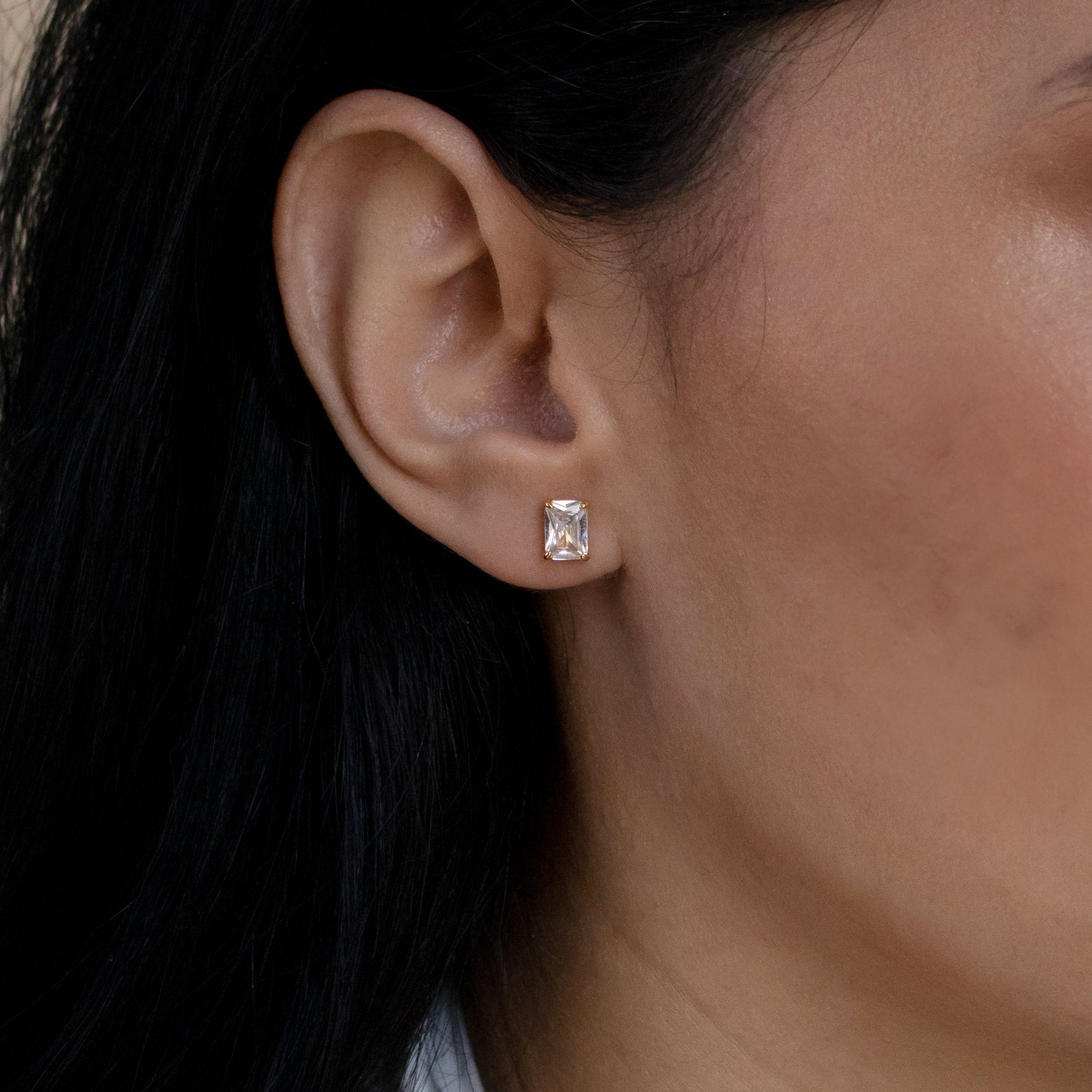 Close-up of a model wearing a gold diamond stud earring with dark hair and skin.