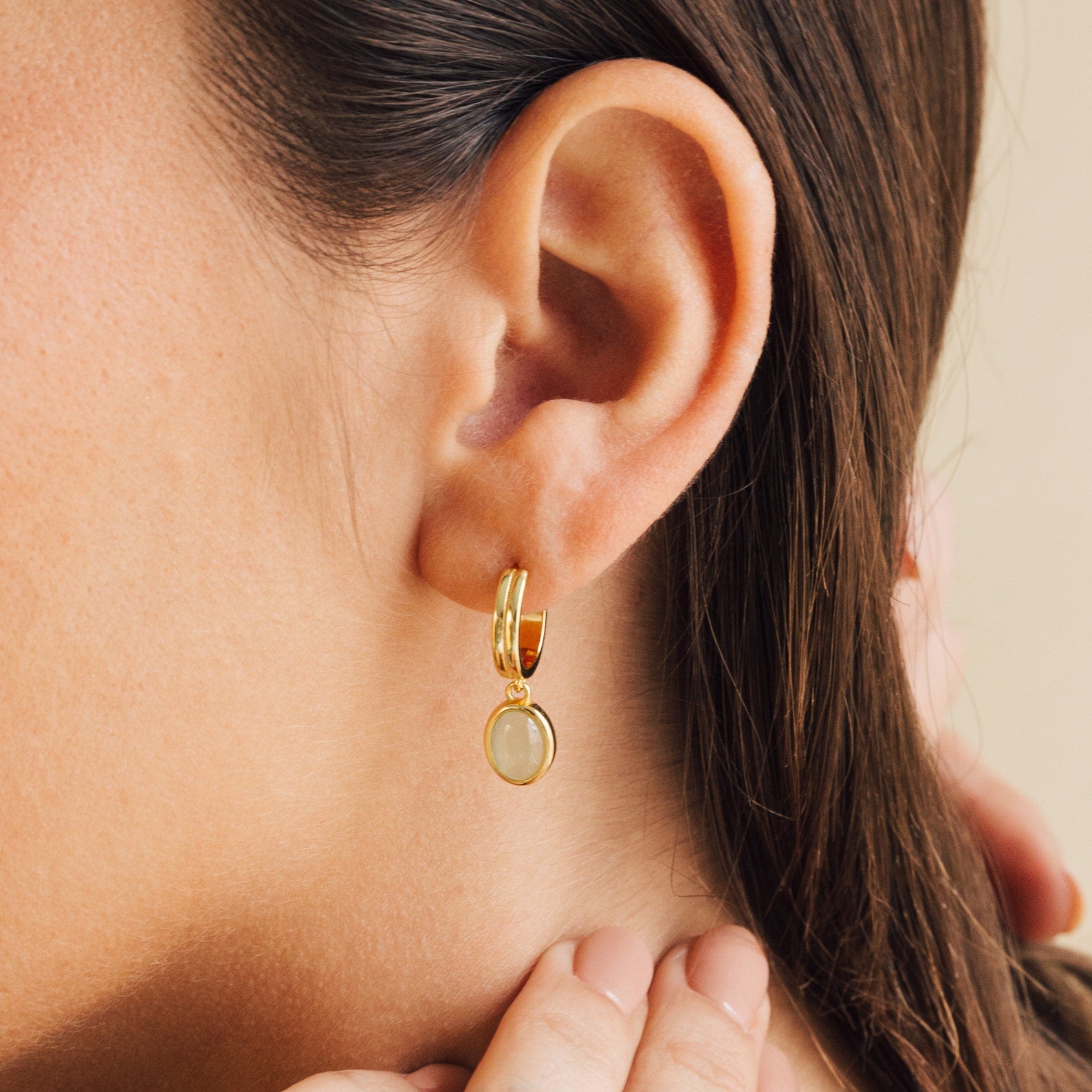 Close-up of a woman wearing a gold hoop earring with a green dangle gemstone.