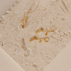 Gold rose necklace and rose earrings on a textured beige surface