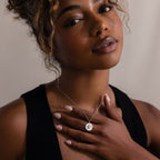 Woman with curly hair in a black top gently touches her Bee Coin Necklace, looking softly at the camera.