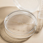 Gold necklace on a clear glass dish with a beige background