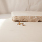 Gold stud earrings with emerald cut diamonds on a beige surface with a neutral background