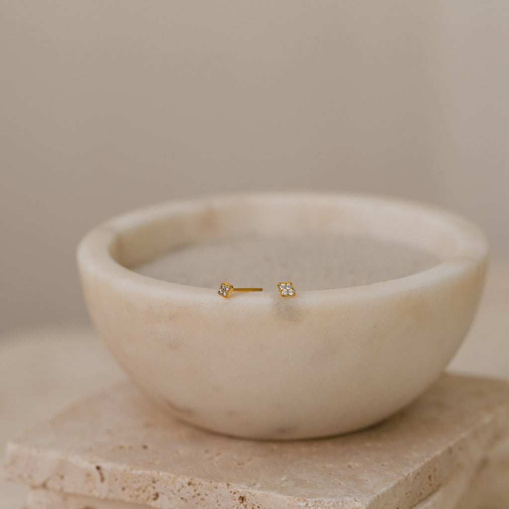 Gold diamond cluster stud earrings in a marble bowl on a neutral background