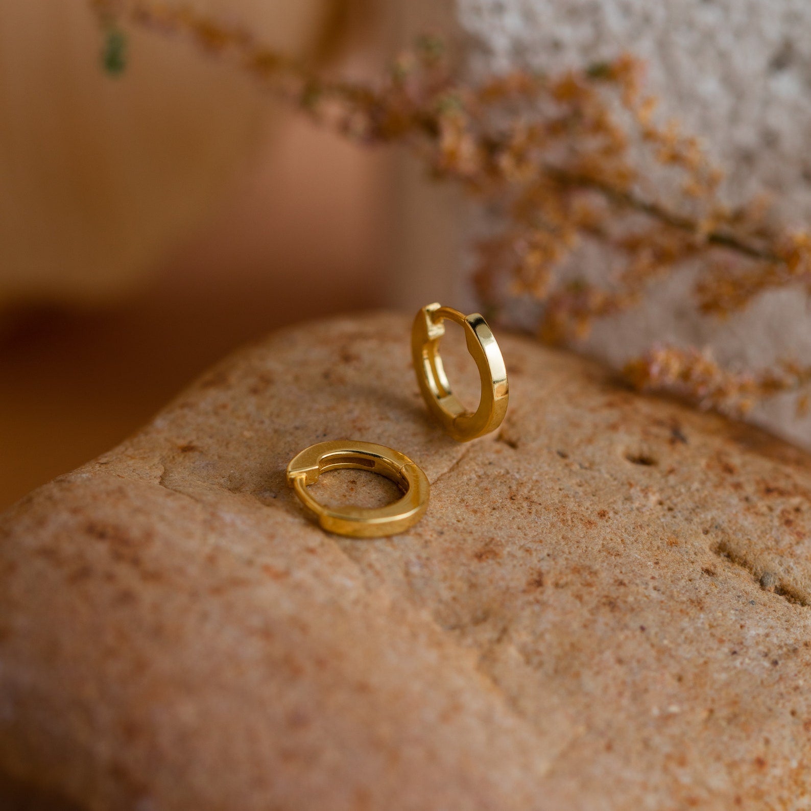 Gold huggie hoop earrings on a textured surface with a blurred natural background
