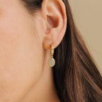 Close-up of a model wearing a gold hoop earring with a small round green pendant.