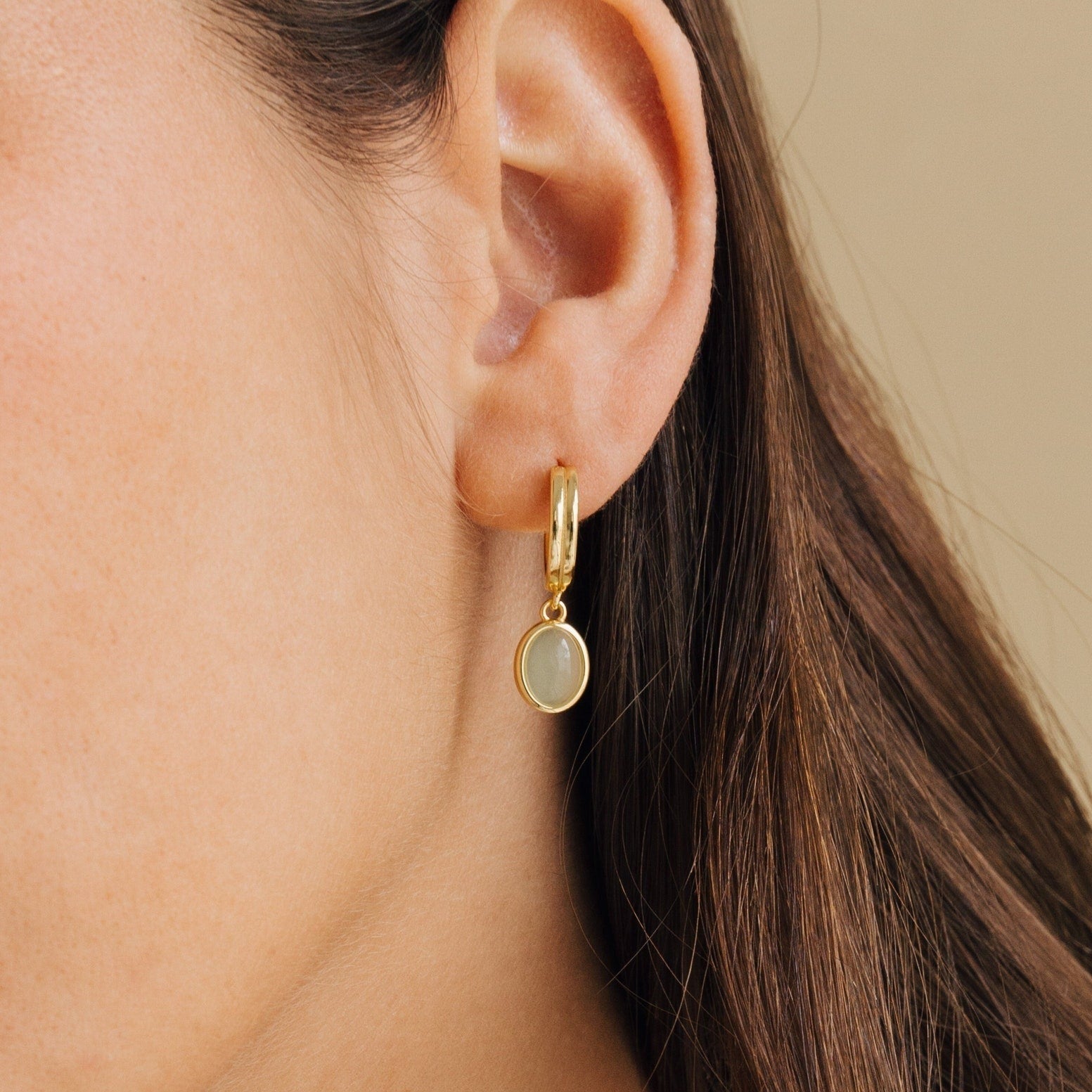 Close-up of a model wearing a gold hoop earring with a small round green pendant.