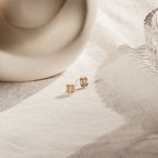 Gold stud earrings with clear gemstones on a textured beige surface