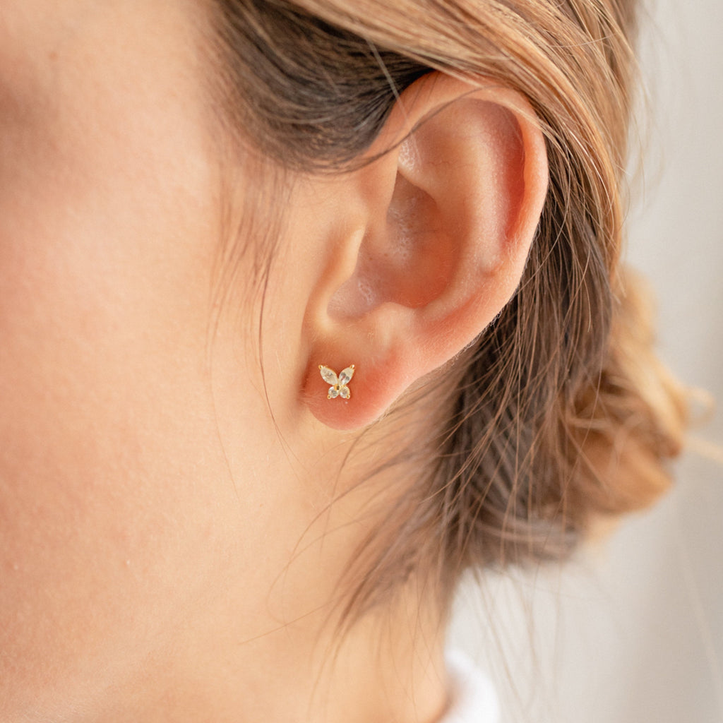 Close-up of a model wearing a gold butterfly earring with a blurred background