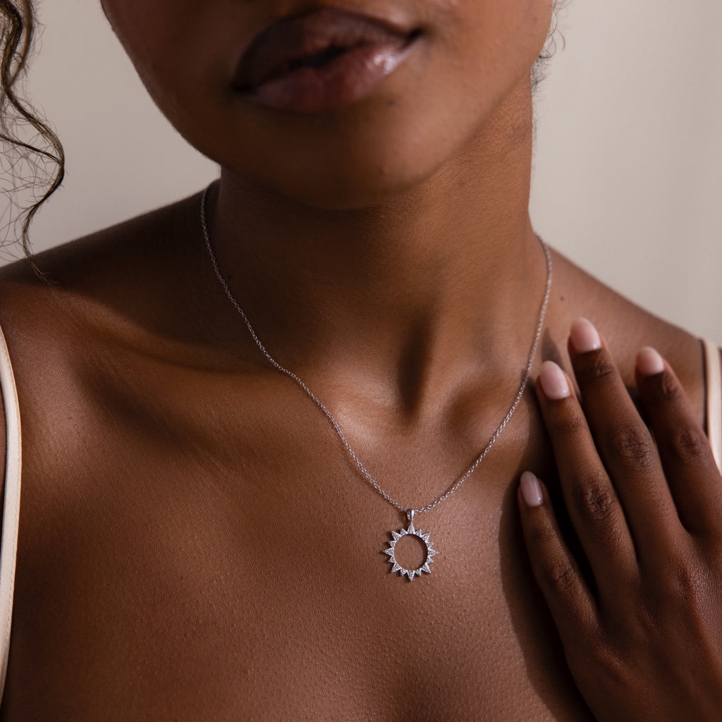A woman gently touches her collarbone while wearing the Pave Sun Necklace adorned with sparkling pave accents.