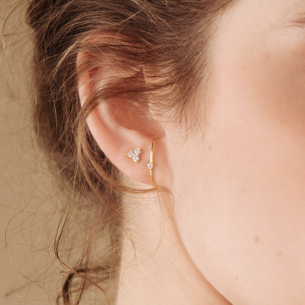 Close-up of an ear wearing a gold earrings with small stones.