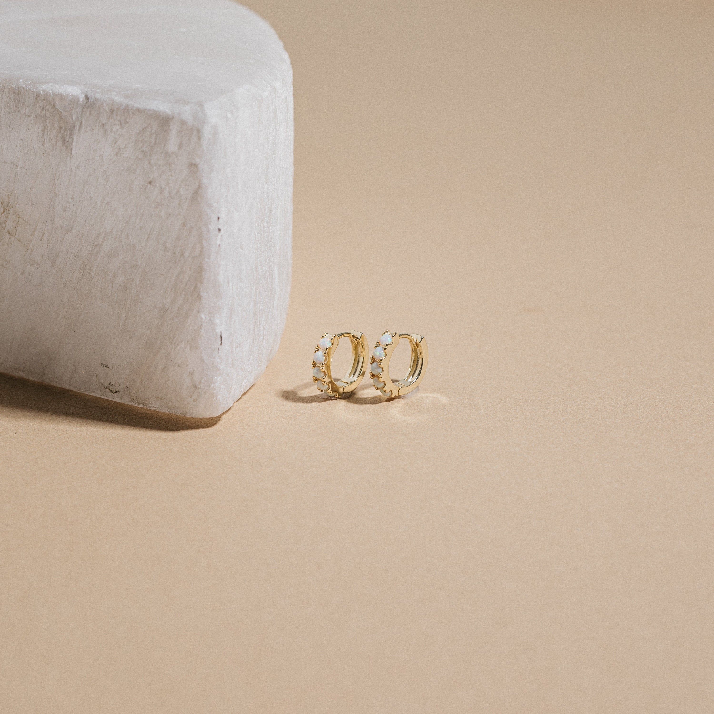 Gold opal hoop earrings on a beige surface with a neutral background