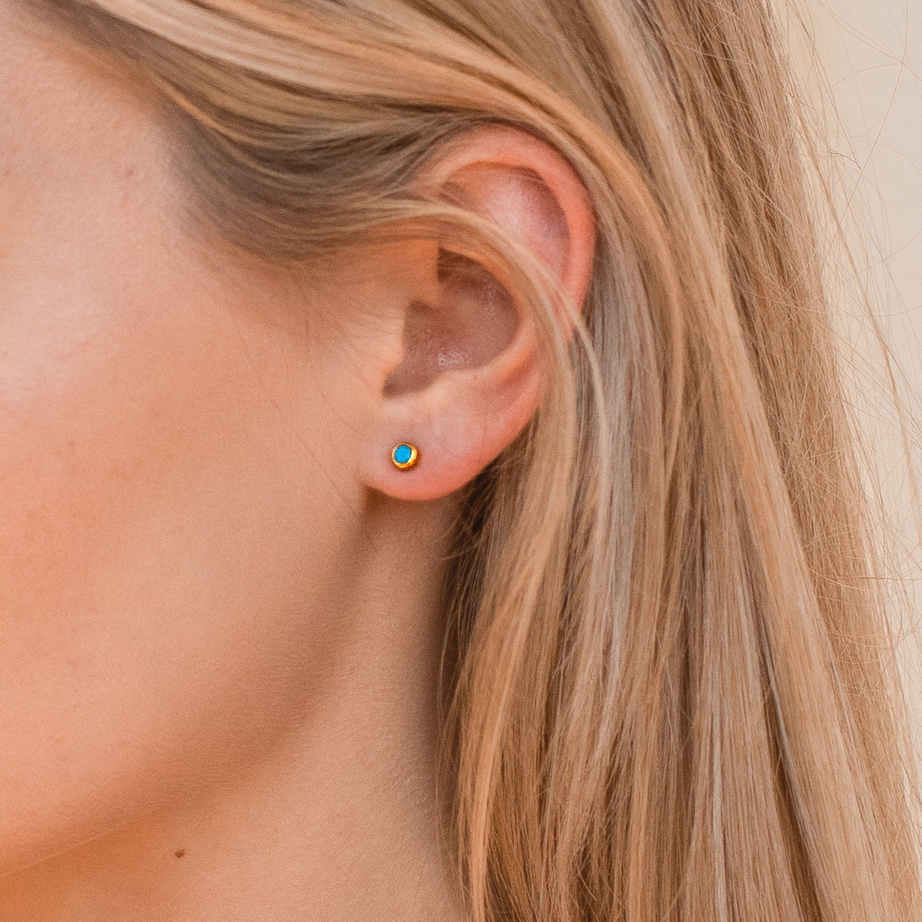 Close-up of a person wearing a colorful turquoise gold stud earring with blonde hair.