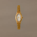 The Grid Chain Timepiece features a gold oval dial, white face, Roman numerals, and a vintage-inspired bracelet on a plain neutral background.
