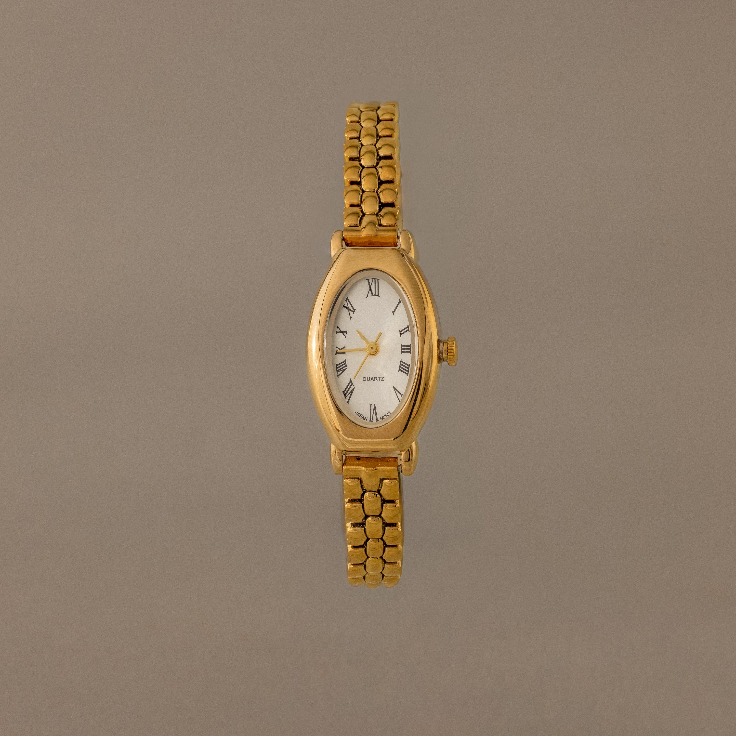The Grid Chain Timepiece features a gold oval dial, white face, Roman numerals, and a vintage-inspired bracelet on a plain neutral background.