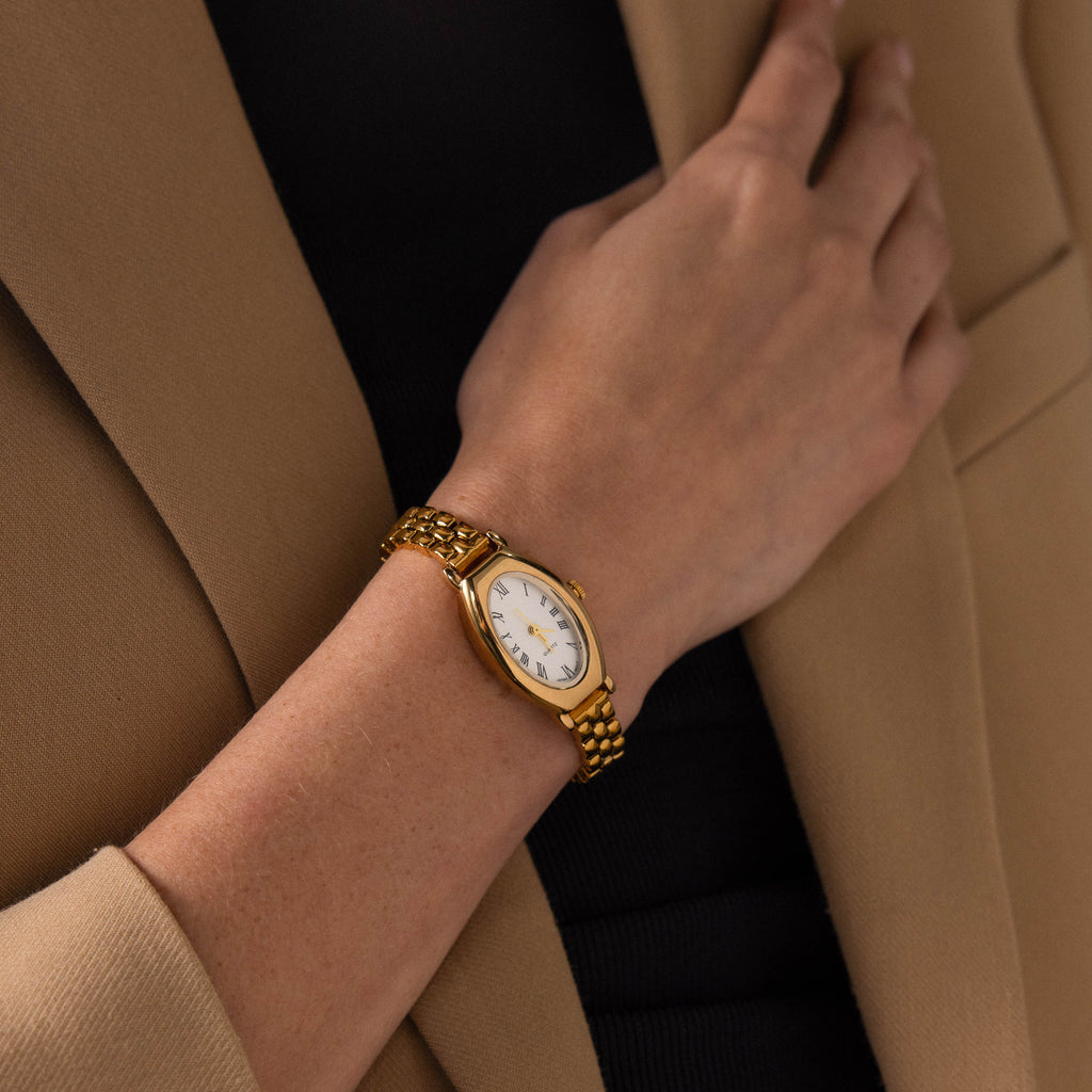 A person wearing the Grid Chain Timepiece with a beige blazer layered over a black top.