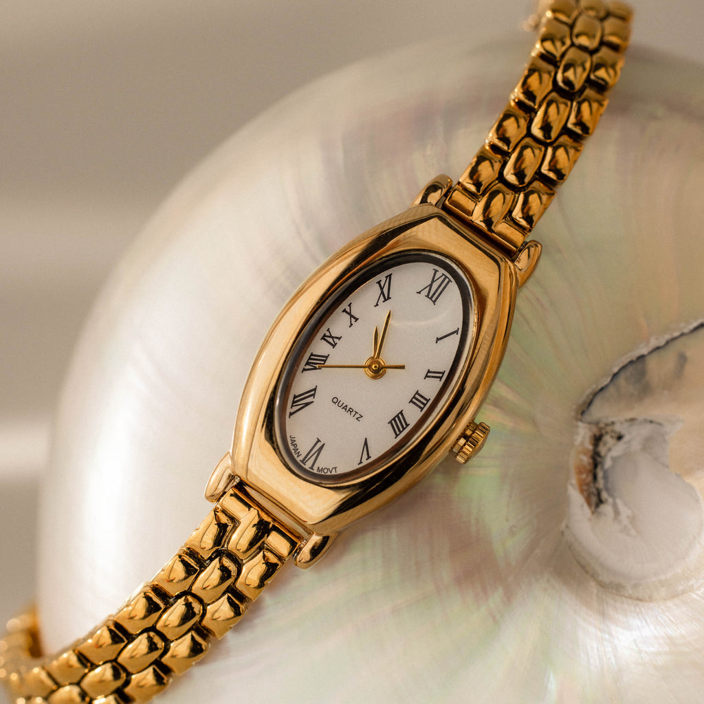 Grid Chain Timepiece with a white face and Roman numerals, showcased on an iridescent seashell for a timeless, elegant look.
