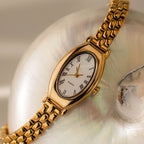 Grid Chain Timepiece with a white face and Roman numerals, showcased on an iridescent seashell for a timeless, elegant look.