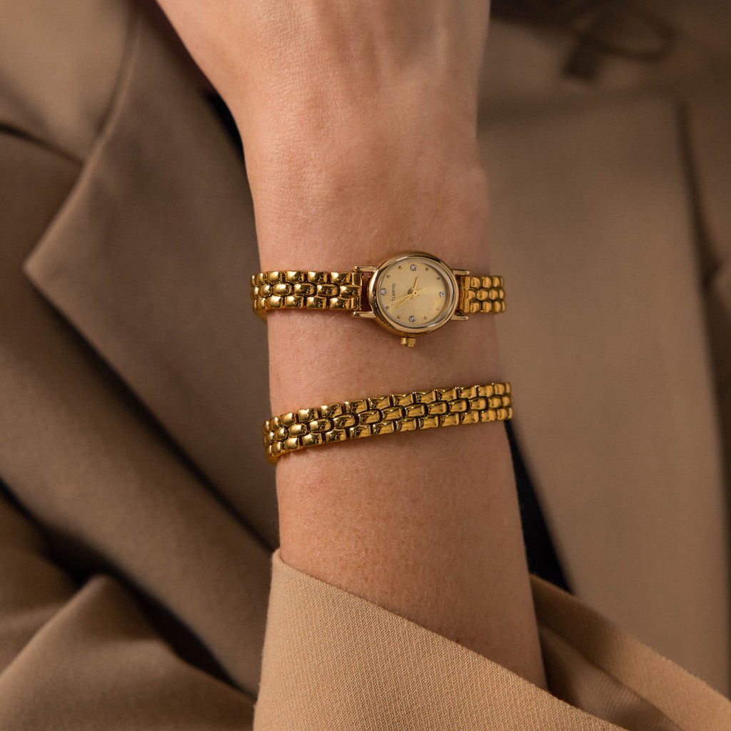 The Oval Link Timepiece Set, with its gold-tone bracelet, adorns the wrist of a person in a beige blazer.