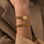 The Oval Link Timepiece Set, with its gold-tone bracelet, adorns the wrist of a person in a beige blazer.