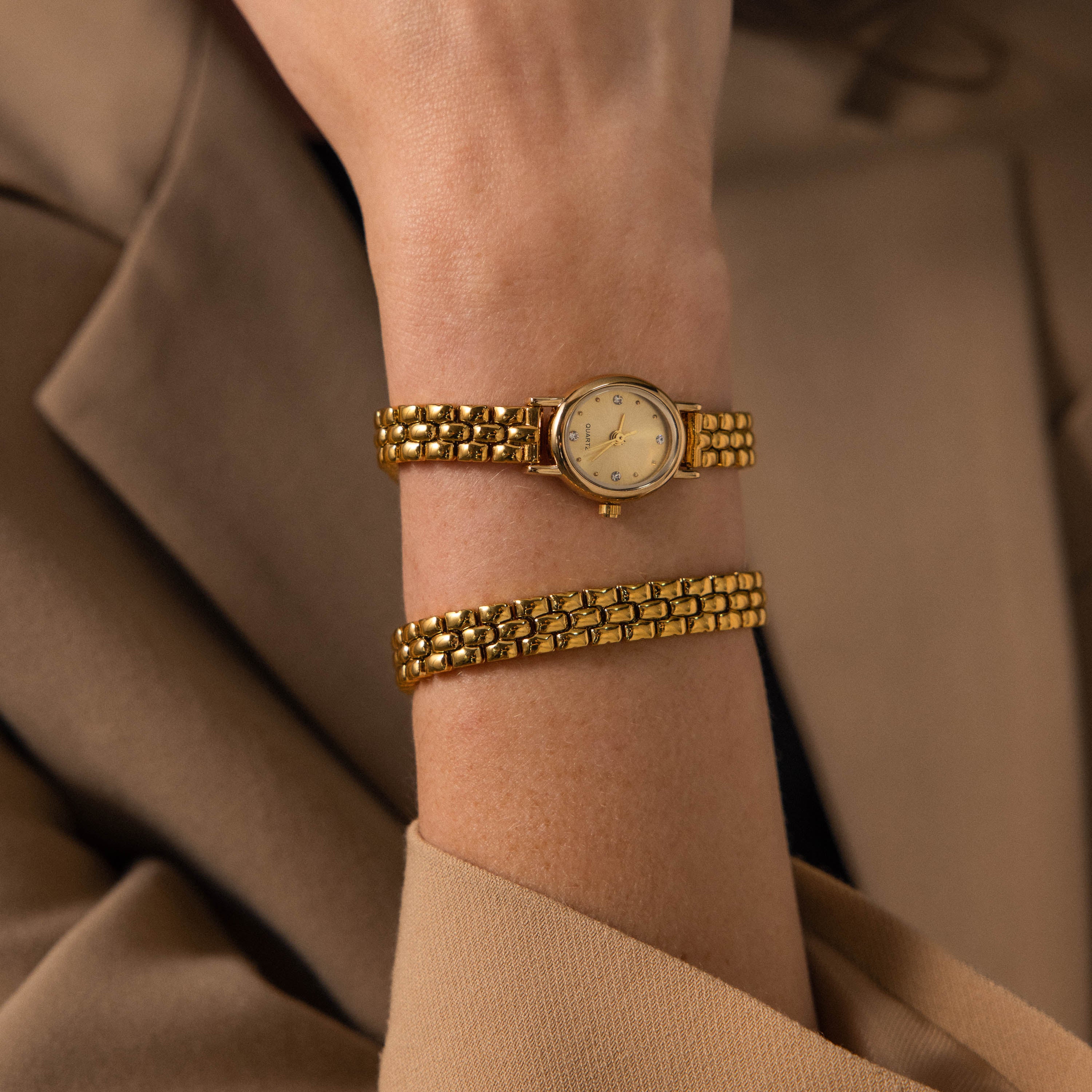 The Oval Link Timepiece Set, with its gold-tone bracelet, adorns the wrist of a person in a beige blazer.