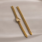The Oval Link Timepiece Set, featuring a gold-tone watch and its detached link bracelet, is showcased on a smooth beige surface for an elegant look.