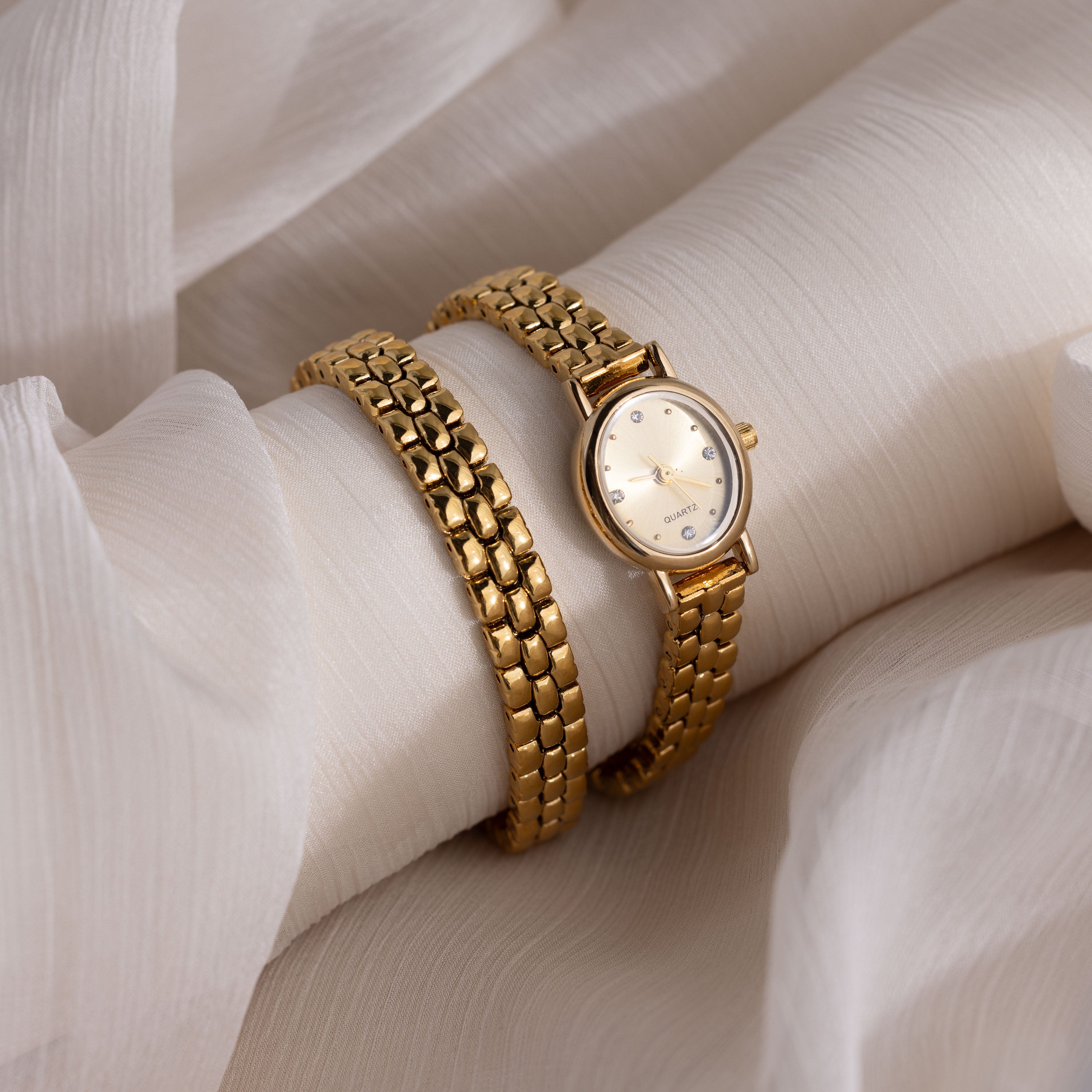 The Oval Link Timepiece Set, including a gold-tone watch and matching link bracelet, rests elegantly on soft white fabric.