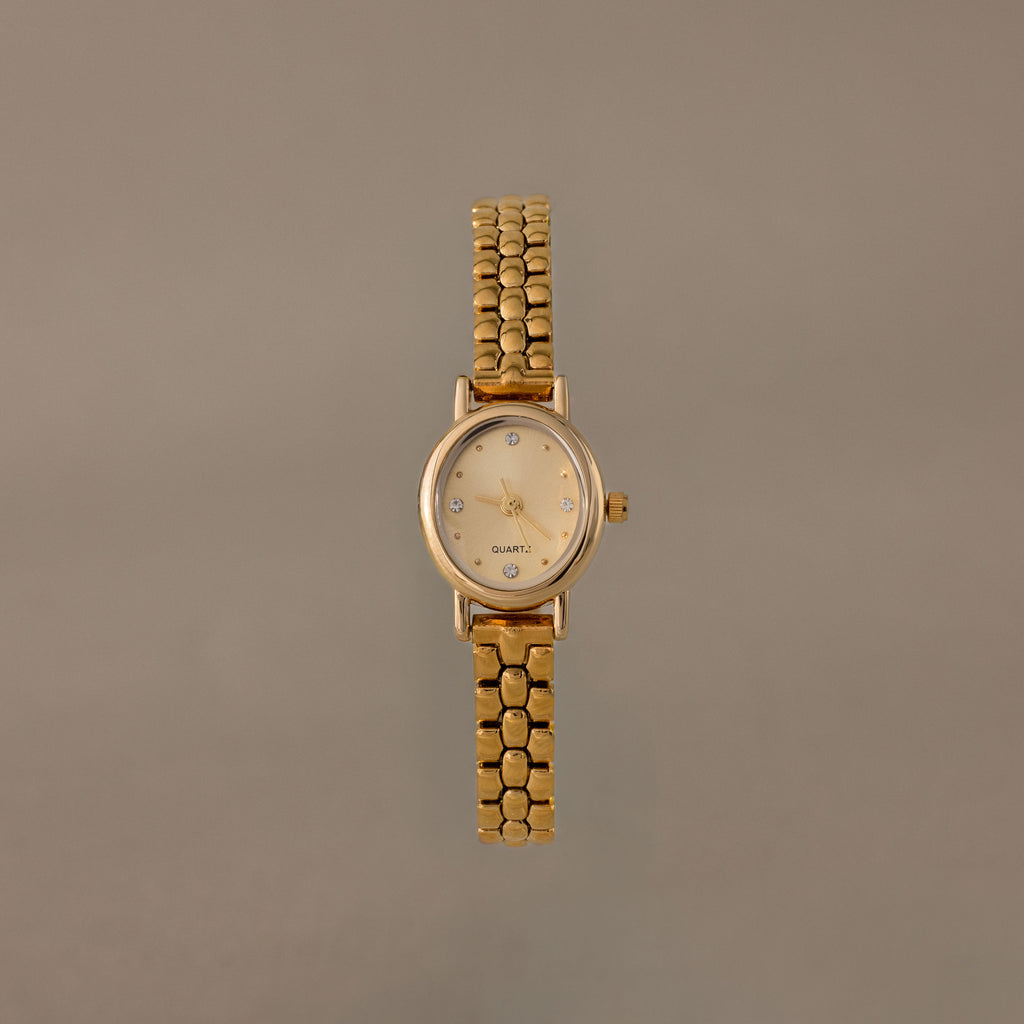 The Oval Link Timepiece Set features a gold-tone watch with a round face and beaded link bracelet, shown against a plain beige background.