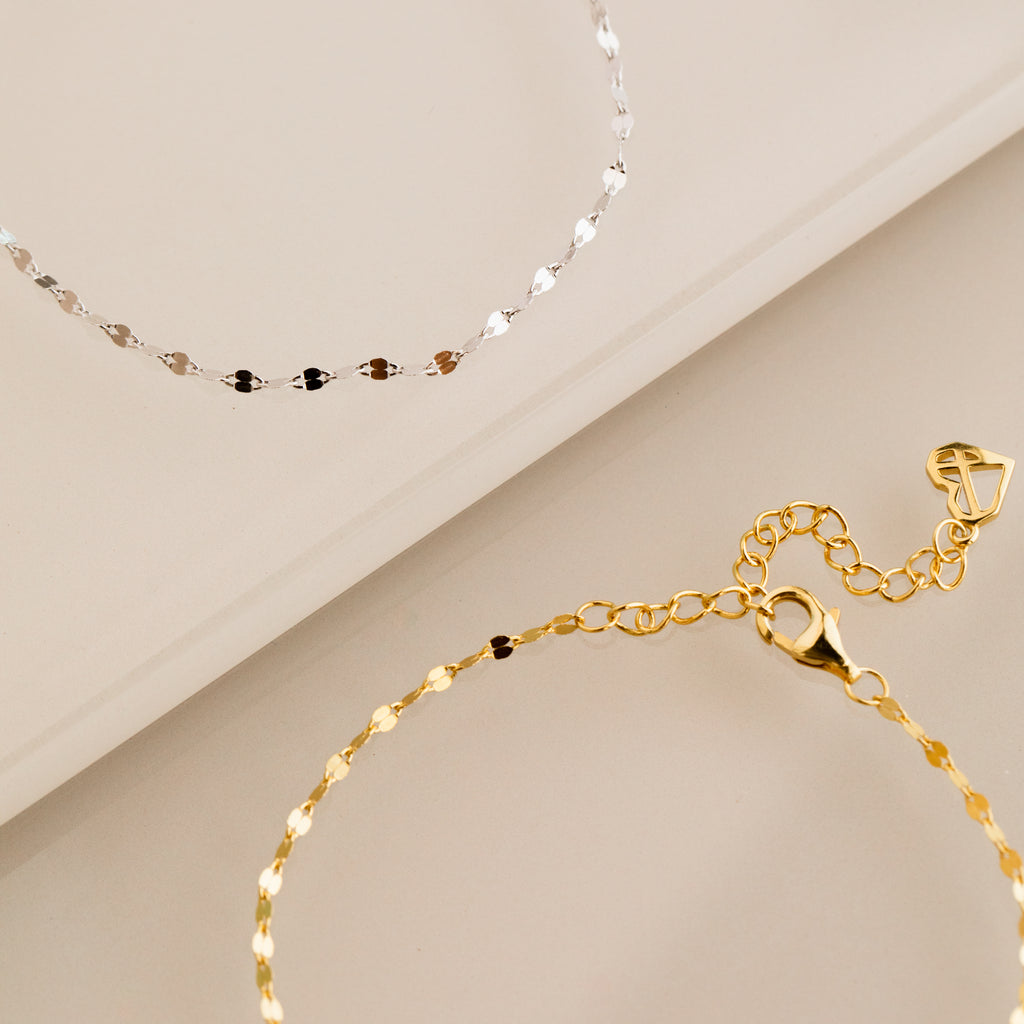 A dainty gold bracelet and the Josephine Chain Bracelet in Sterling Silver are elegantly displayed on a beige surface.