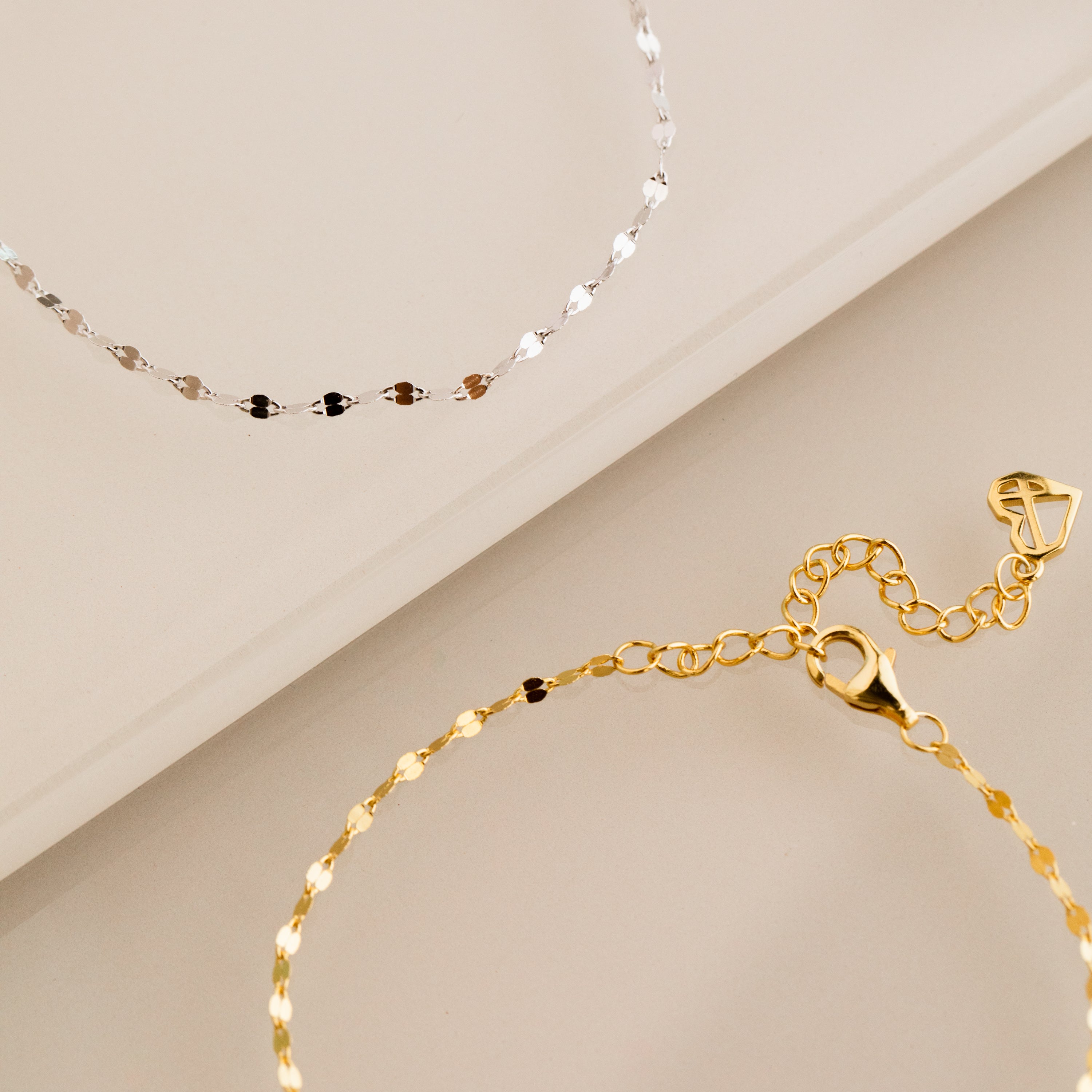 A dainty gold bracelet and the Josephine Chain Bracelet in Sterling Silver are elegantly displayed on a beige surface.