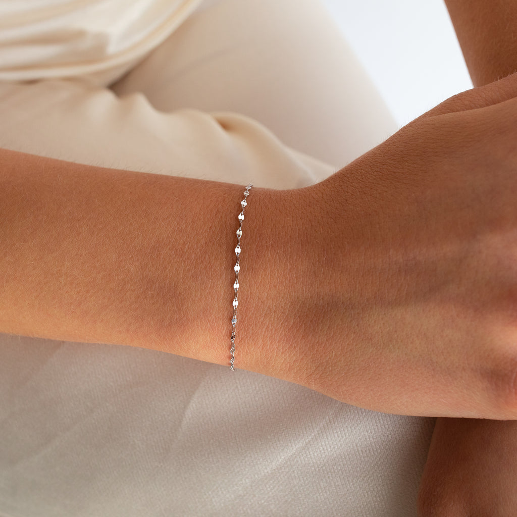 The Josephine Chain Bracelet in Sterling Silver features delicate, shining silver links that elegantly grace the wrist against a cream-colored background.