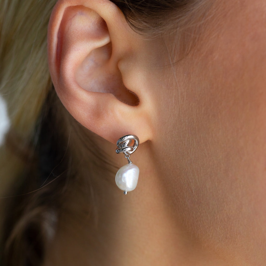 A close-up of a woman's ear adorned with Knot Pearl Drop Earrings in Sterling Silver.
