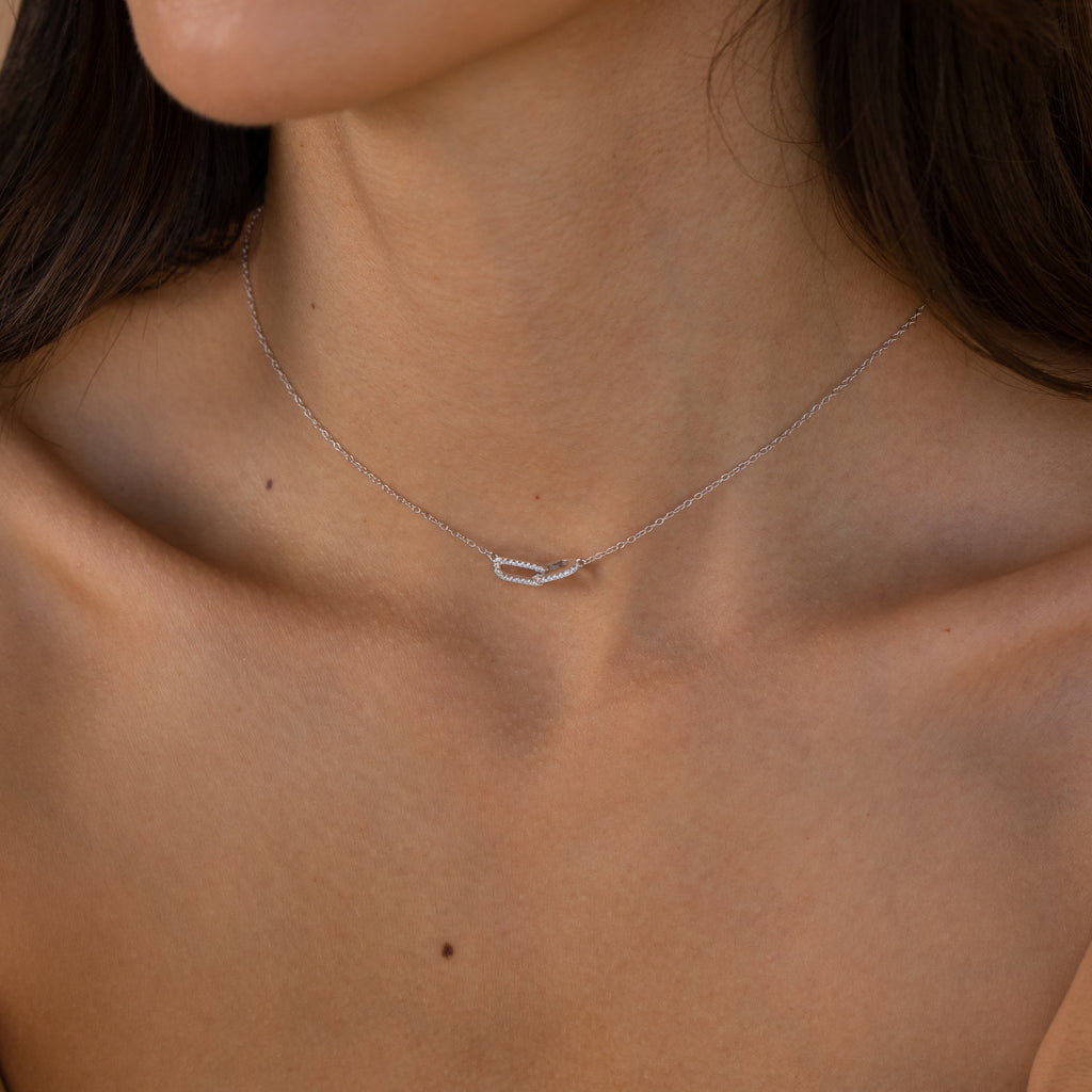 A woman wears the Pave Linked Pendant Necklace—a delicate silver charm necklace with a curved pendant—adorning her bare neck and shoulders.