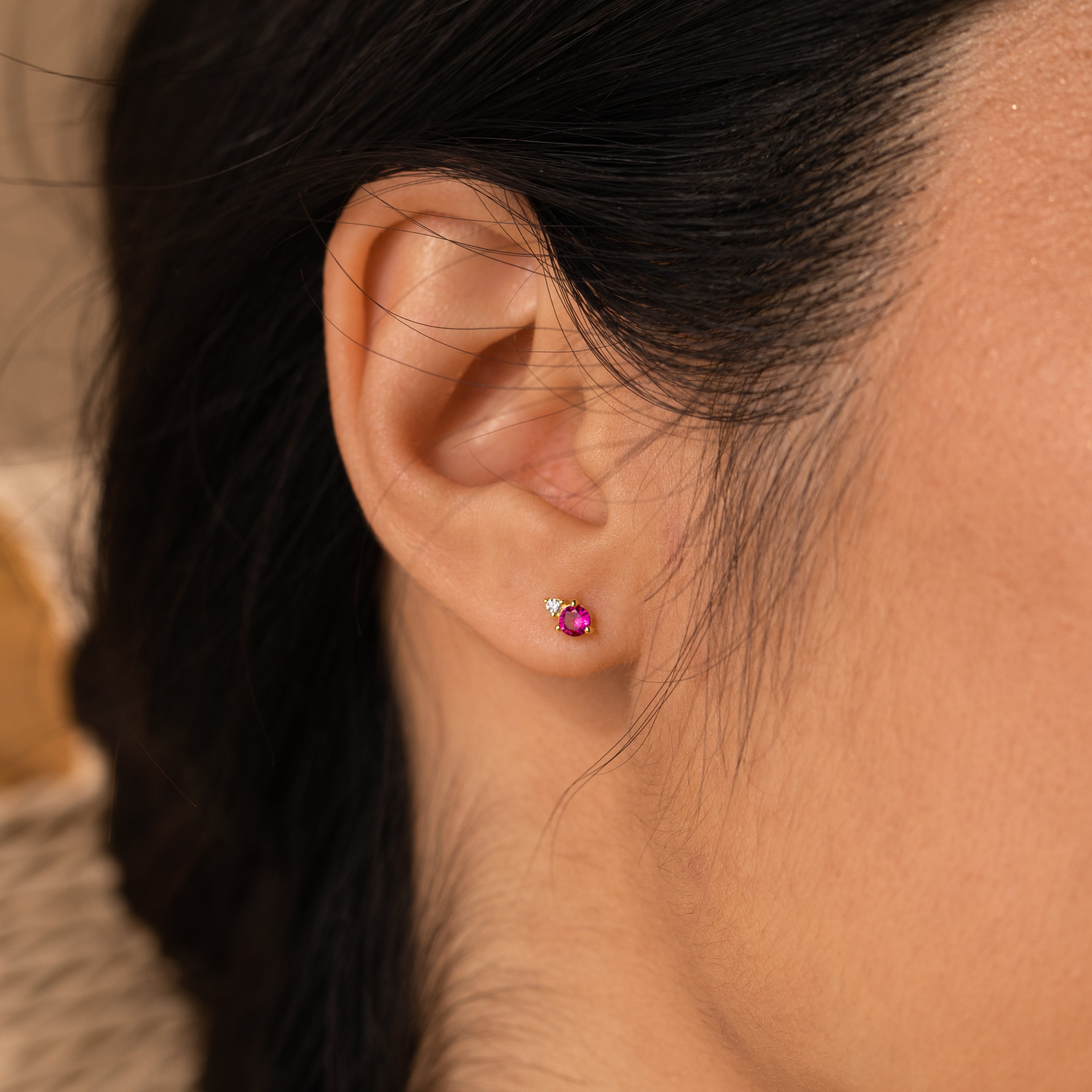 Close-up of a womans ear wearing Raindrop Amethyst Studs—dainty earrings featuring a small amethyst stone and a tiny clear gemstone accent.