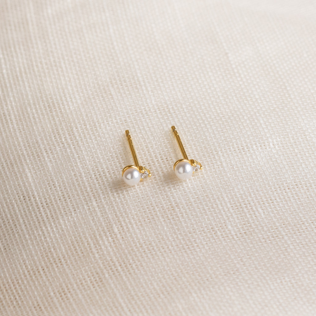 Raindrop Pearl Studs, perfect as dainty earrings or birthstone studs, are displayed on a textured cream fabric background.