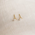 Raindrop Pearl Studs, perfect as dainty earrings or birthstone studs, are displayed on a textured cream fabric background.