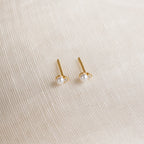 Raindrop Pearl Studs, perfect as dainty earrings or birthstone studs, are displayed on a textured cream fabric background.
