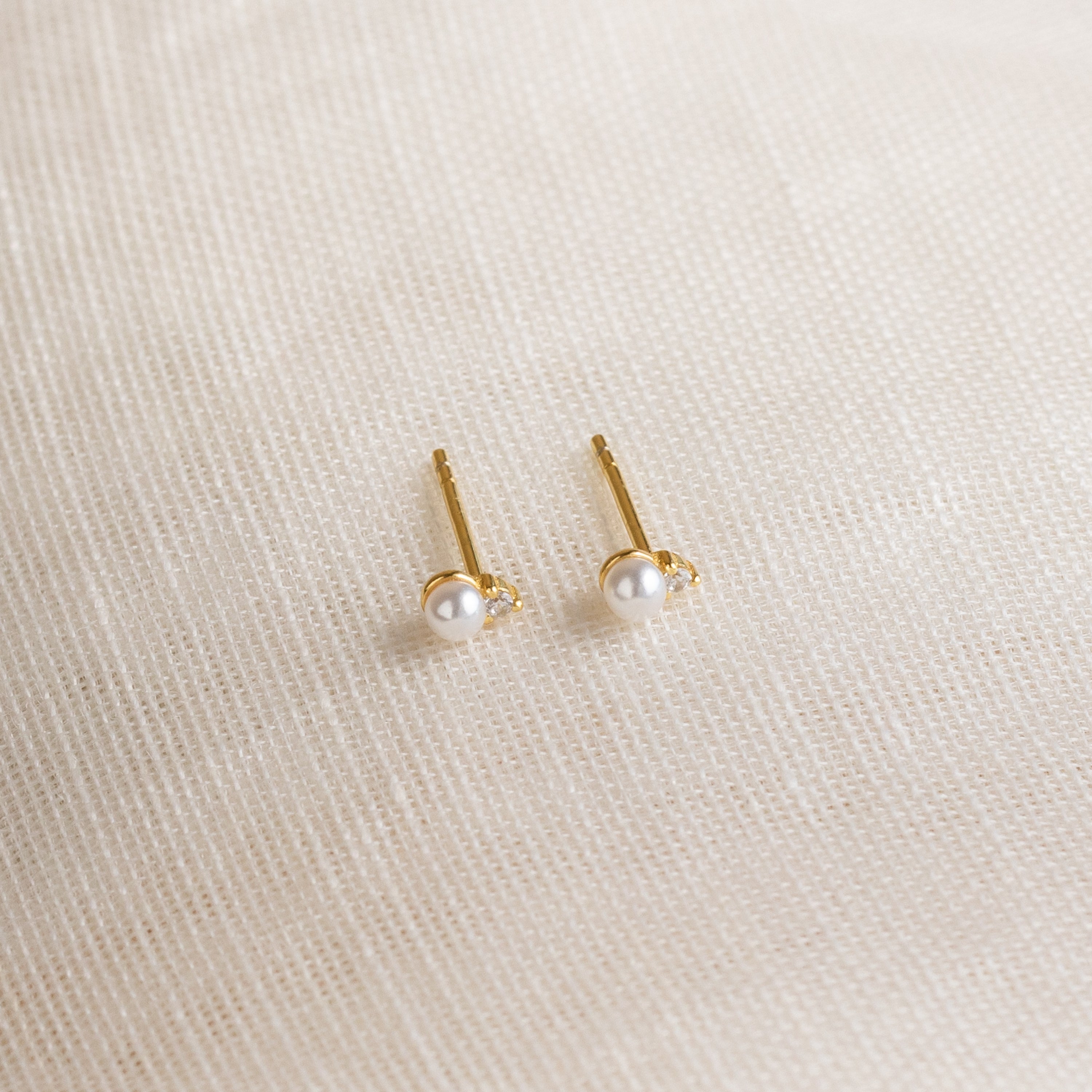 Raindrop Pearl Studs, perfect as dainty earrings or birthstone studs, are displayed on a textured cream fabric background.