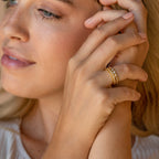 A blonde woman displays a stylish Thin Stacking Rings Set in 18K Gold on her hand beside her face—an elegant Christmas gift idea.