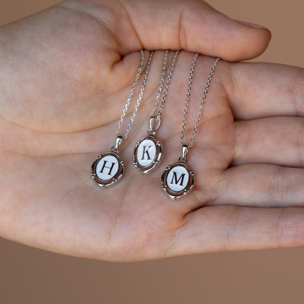 A hand holds three Initial Pendant Necklaces in Sterling Silver, each featuring a pendant with the letter H, K, and M.