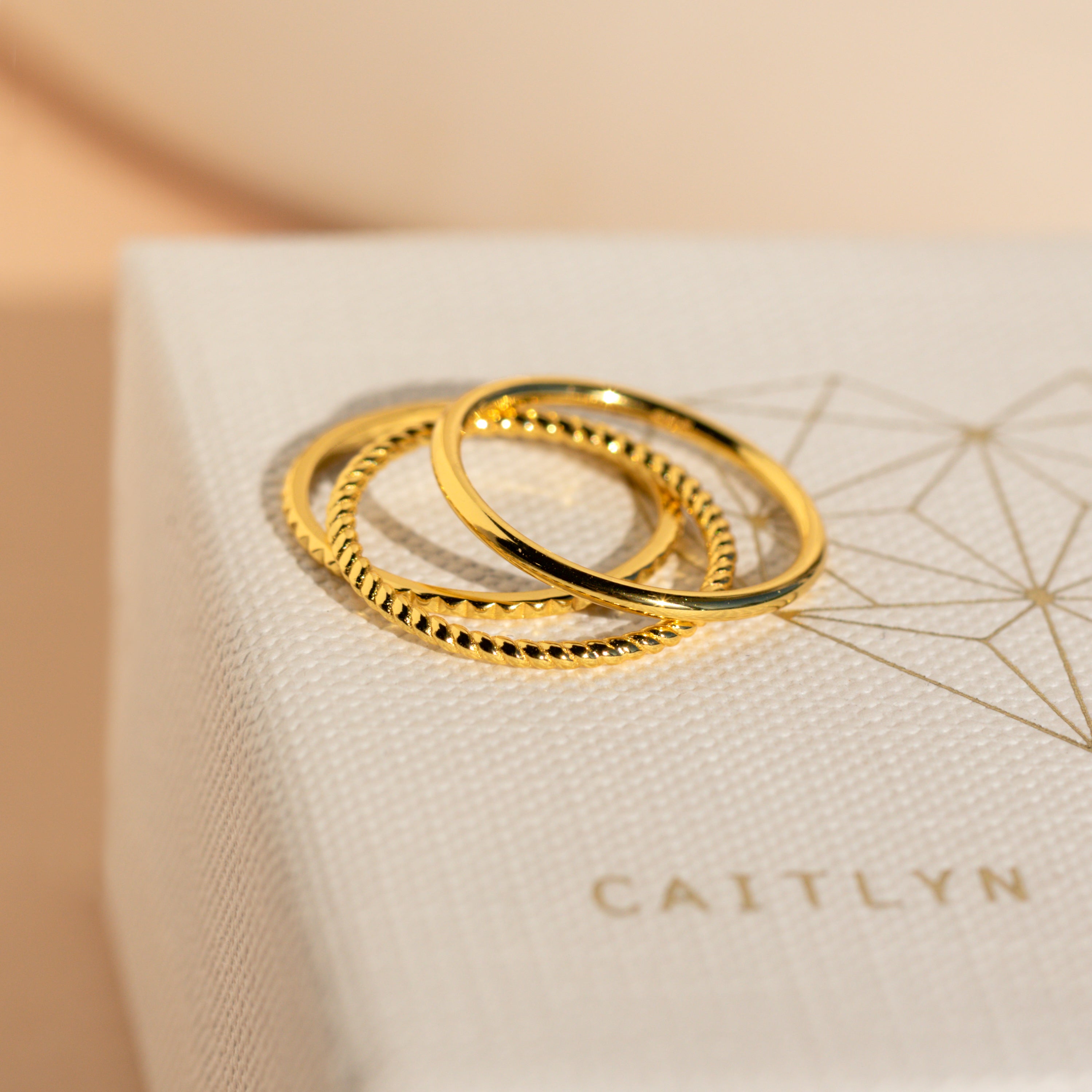 Two gold rings from the Thin Stacking Rings Set—one smooth, one textured—are displayed on a white box, making them ideal for stacking or as a thoughtful Christmas gift.