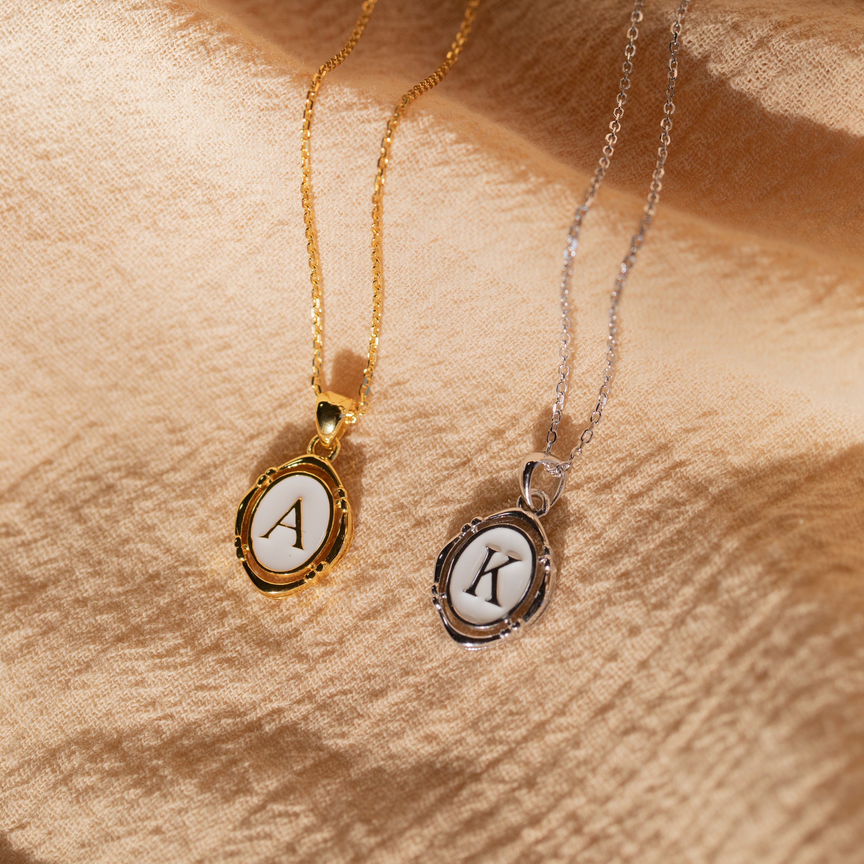 Initial Pendant Necklace in Gold with the letter A and White Gold with the letter K in a vintage serif font lay side by side.