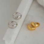 The Olivia Hoops in Sterling Silver—chunky, modern earrings—are displayed on a white marble surface, perfect for adding a contemporary touch to any outfit.