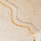 Close-up of delicate gold and silver chain necklaces displayed on a textured beige surface, featuring the Josephine Chain Bracelet in Sterling Silver.
