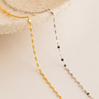 The Josephine Chain Bracelet, a delicate gold and silver beaded design, is displayed draped over a textured white ceramic dish on a neutral background.