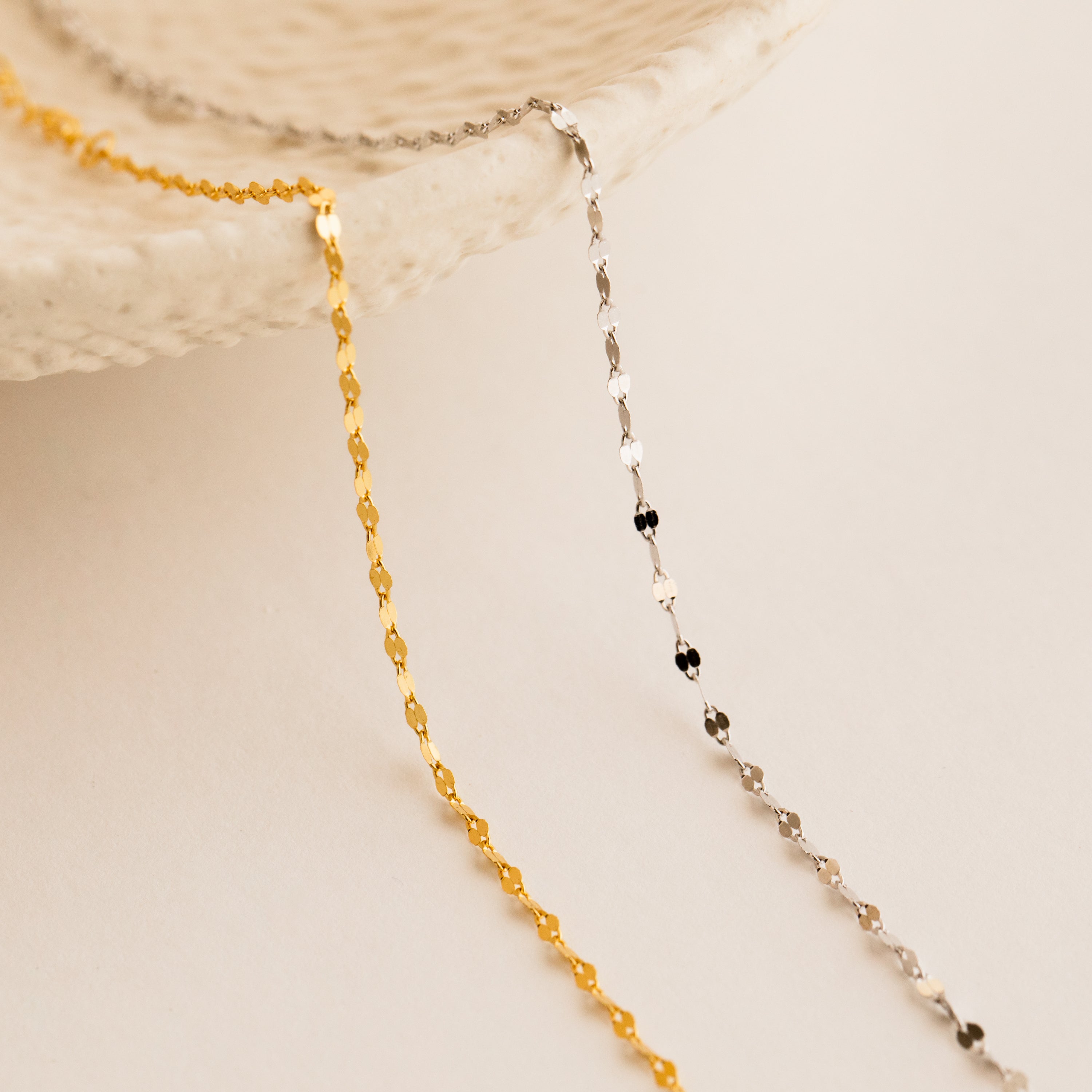 The Josephine Chain Bracelet, a delicate gold and silver beaded design, is displayed draped over a textured white ceramic dish on a neutral background.