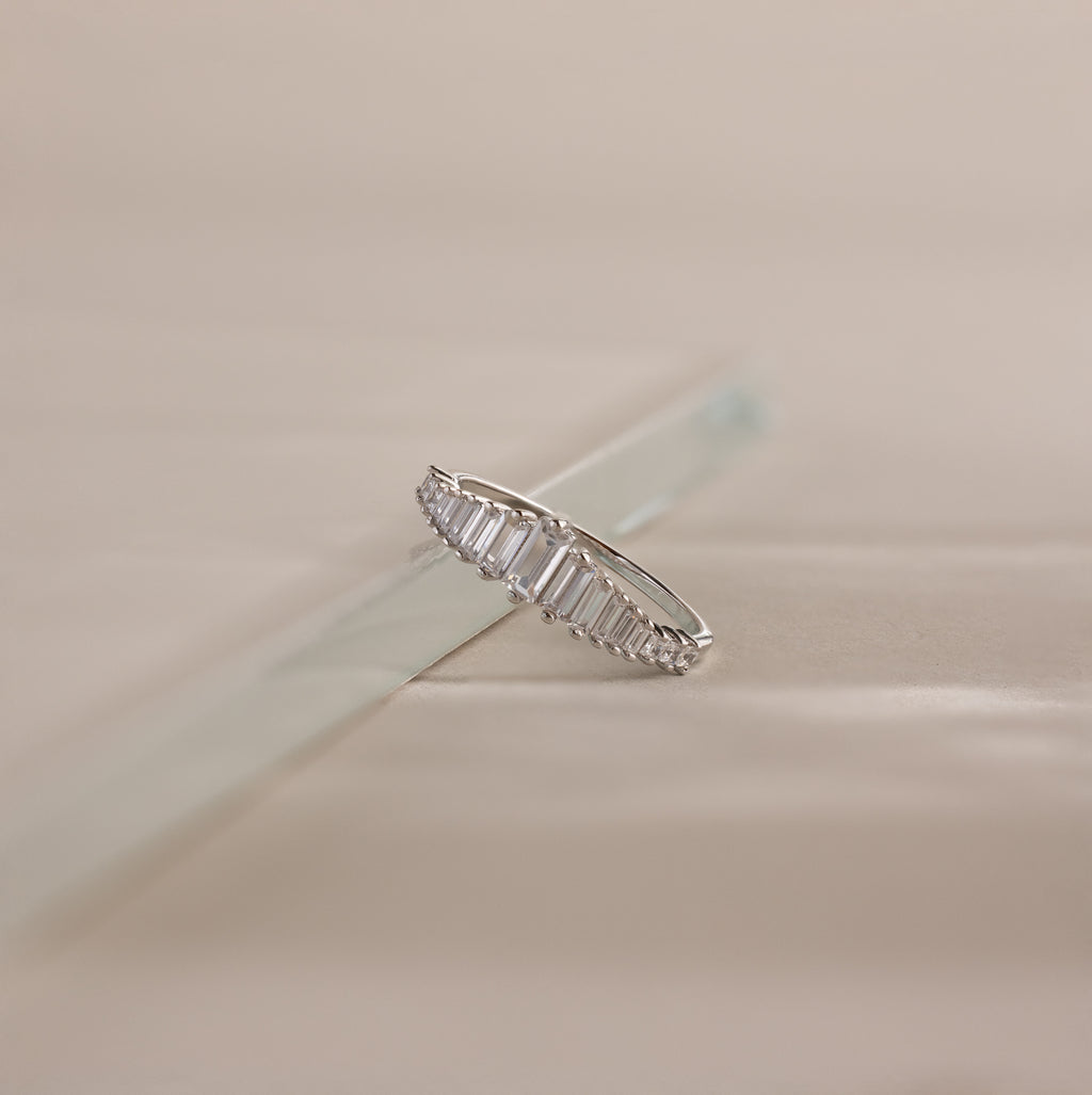 Art Deco Diamond Ring in Sterling Silver with baguette-cut stones displayed on a light, reflective surface, casting a chandelier-like silhouette against a neutral background.