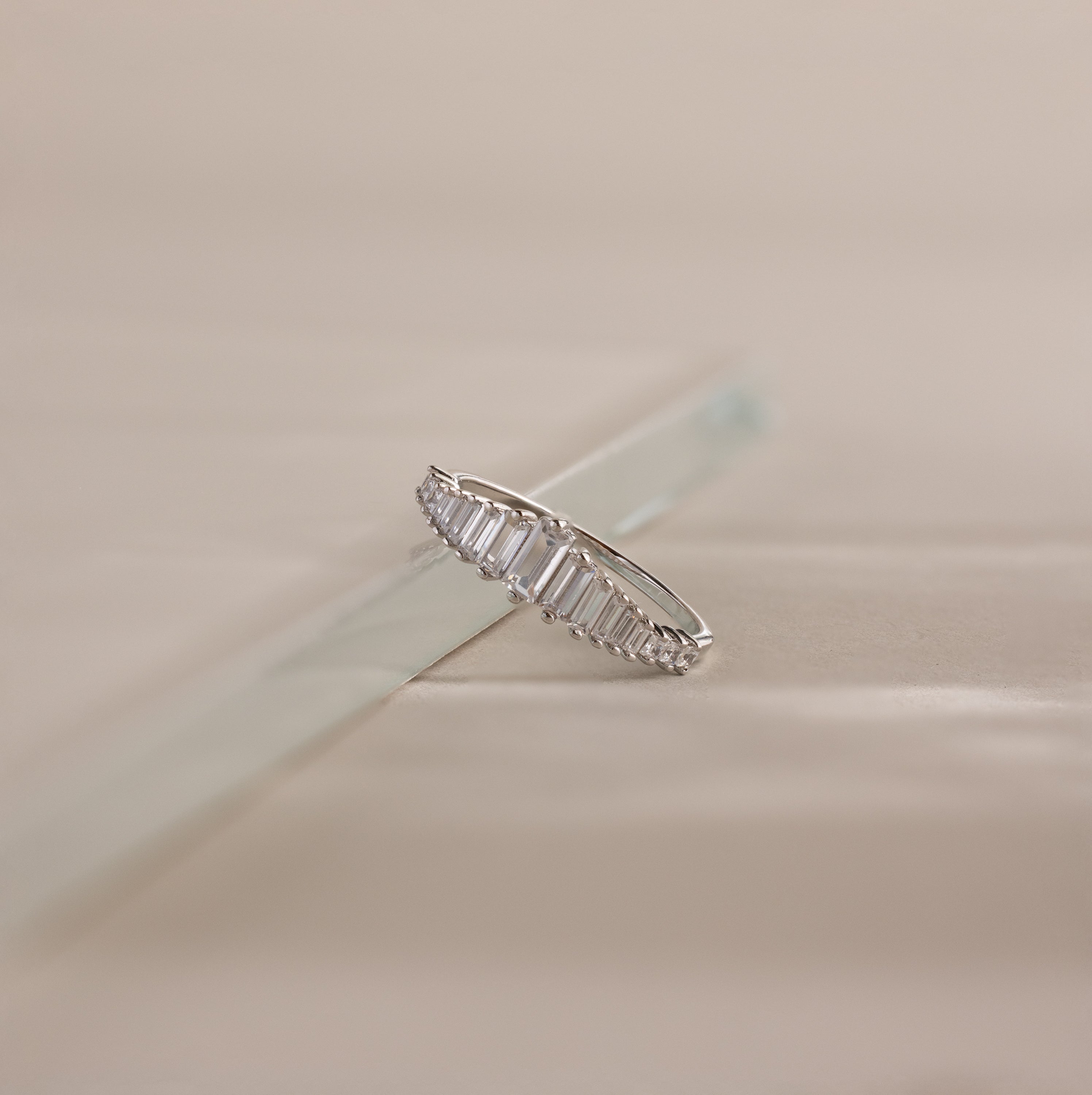 Art Deco Diamond Ring in Sterling Silver with baguette-cut stones displayed on a light, reflective surface, casting a chandelier-like silhouette against a neutral background.