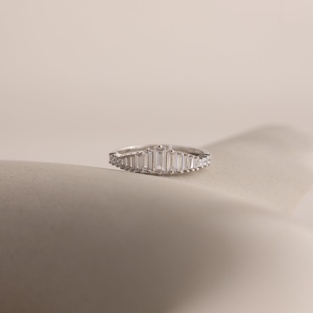The Art Deco Diamond Ring in Sterling Silver features baguette-cut clear stones in a chandelier-inspired design, elegantly displayed on a soft, neutral background.