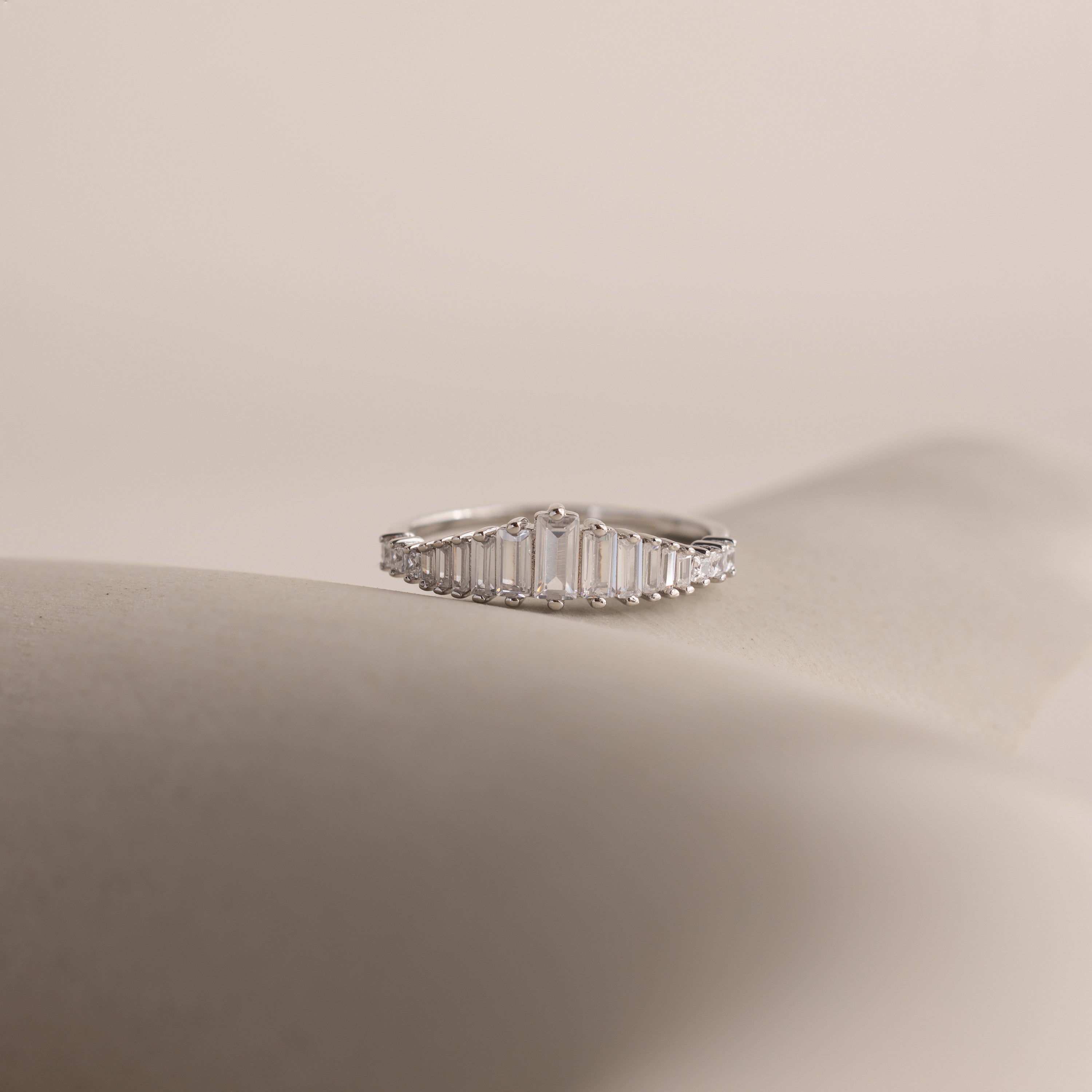 The Art Deco Diamond Ring in Sterling Silver features baguette-cut clear stones in a chandelier-inspired design, elegantly displayed on a soft, neutral background.